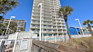 Un hotel de varios pisos con balcones, una zona de piscina y palmeras.