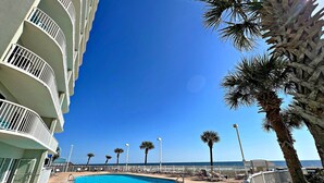 Un área de piscina con cielo azul despejado, piscina, sillas de descanso y palmeras.