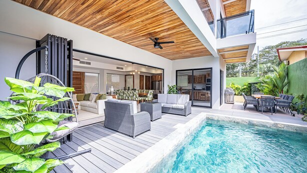 A modern outdoor pool area with wooden decking, outdoor furniture, and a view of the house. - Brand New 7 Bedroom Luxury Villa Prime Location on the South End of Jaco Beach (Jaco)