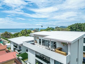 A modern building with a flat roof, large windows, and a balcony with outdoor furniture.