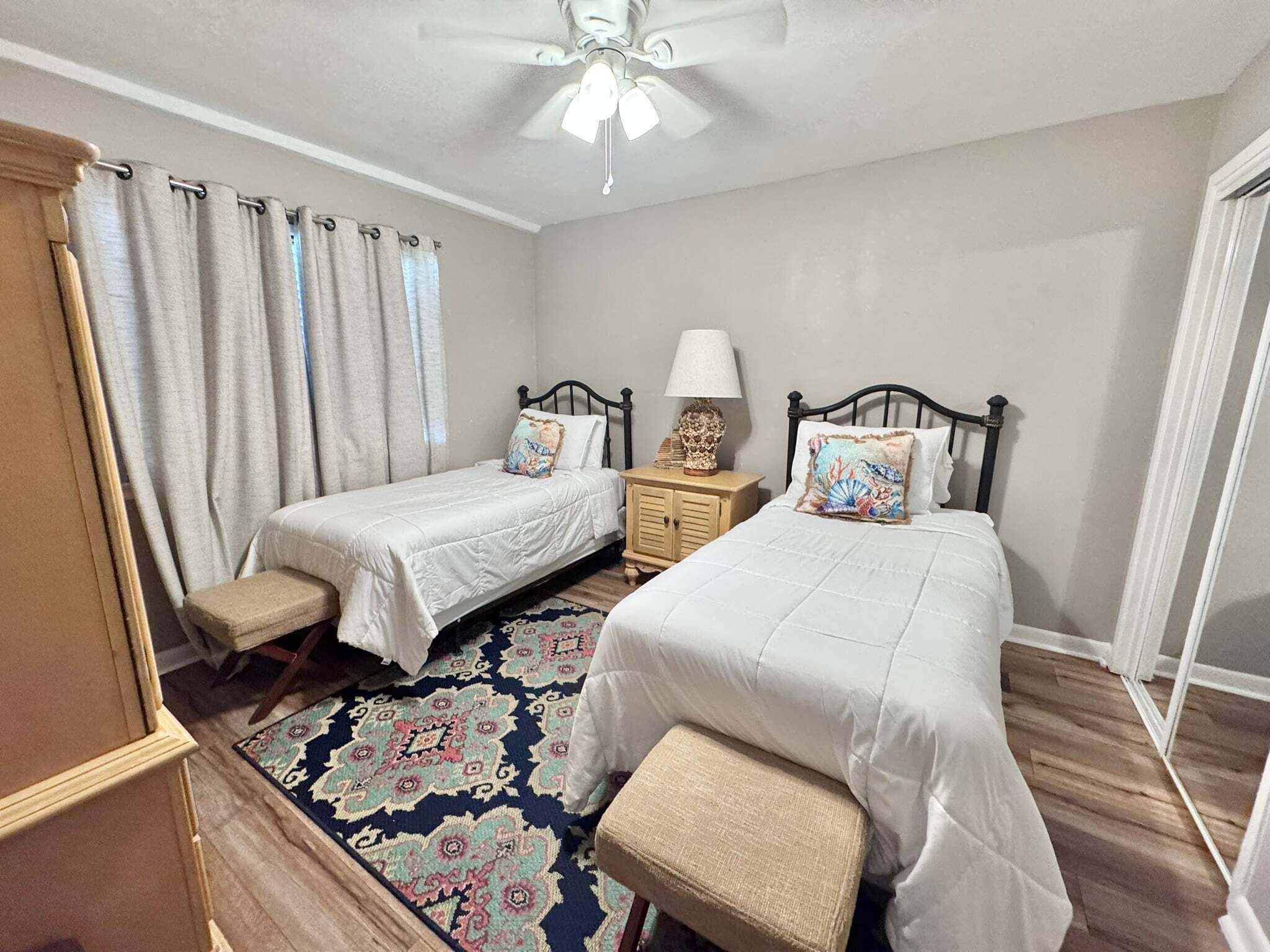 Une chambre avec deux lits, un ventilateur de plafond, une table de chevet avec une lampe et un tapis à motifs.
