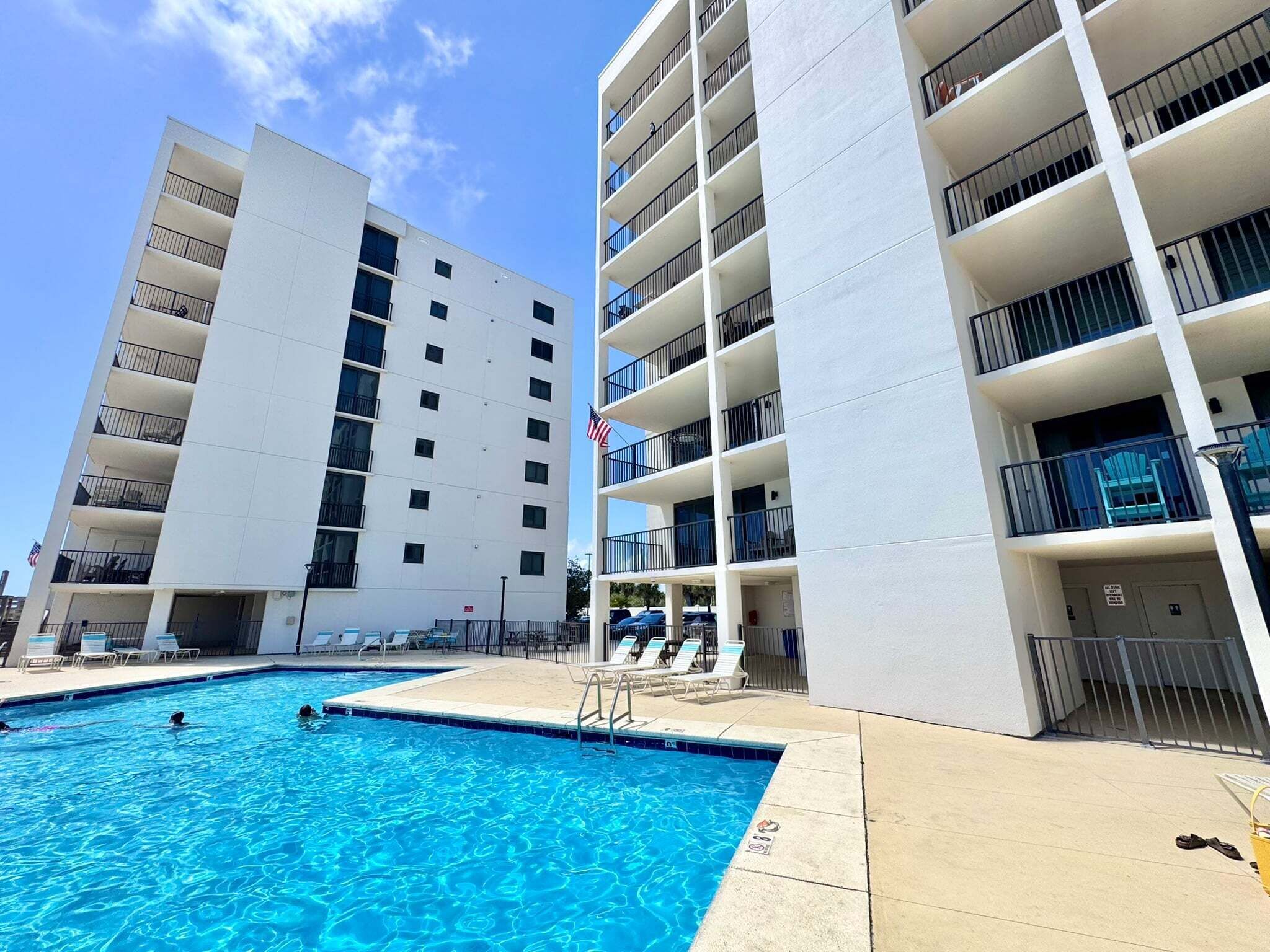 Un hotel de varios pisos con balcones, piscina y sillones de descanso.