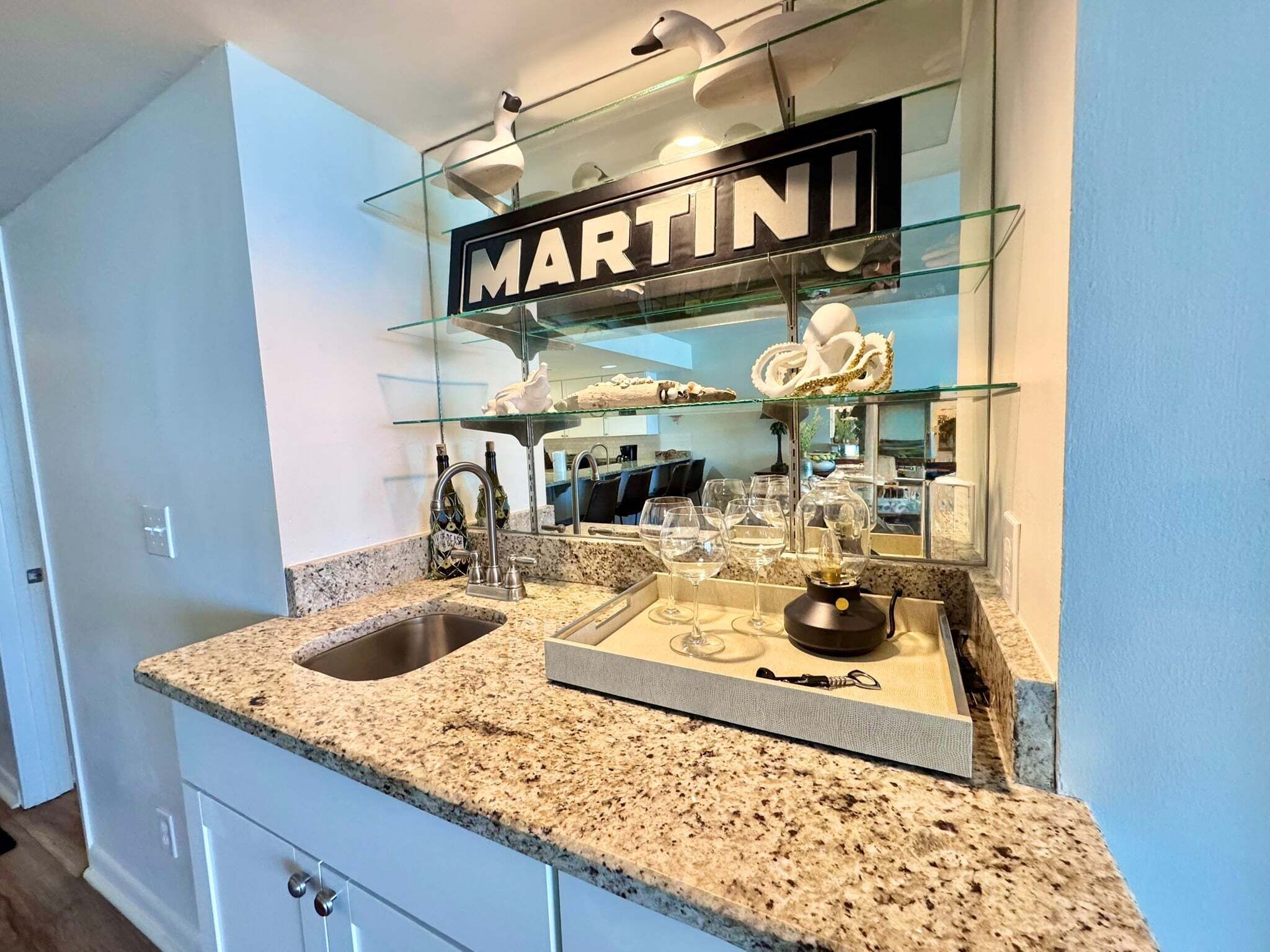 A kitchen with a granite countertop, a double sink, and a glass display case with a 'MARTINI' sign.