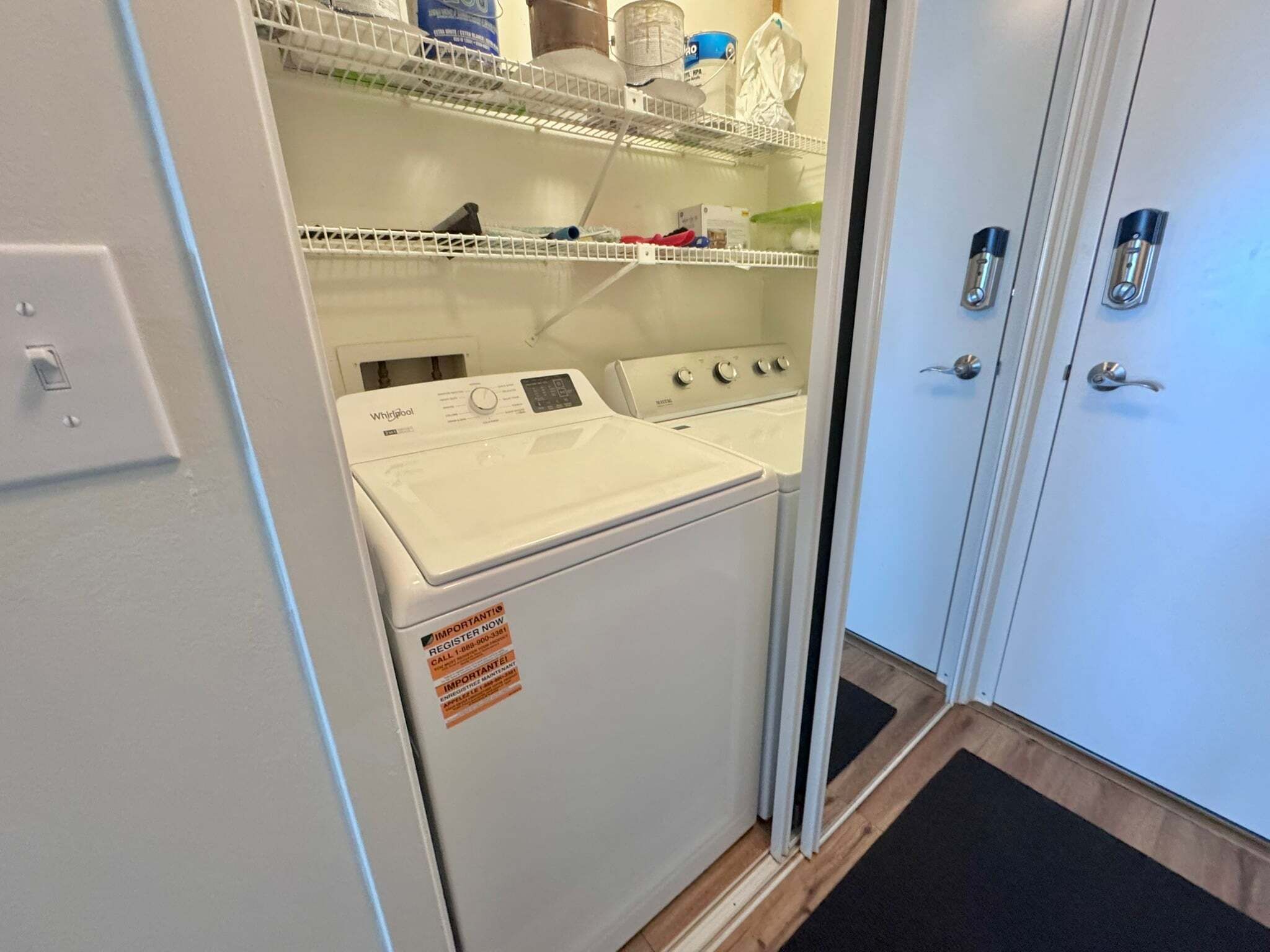 A laundry room with a Whirlpool washer and dryer, a metal shelf with cleaning supplies, and a door with a doorknob.