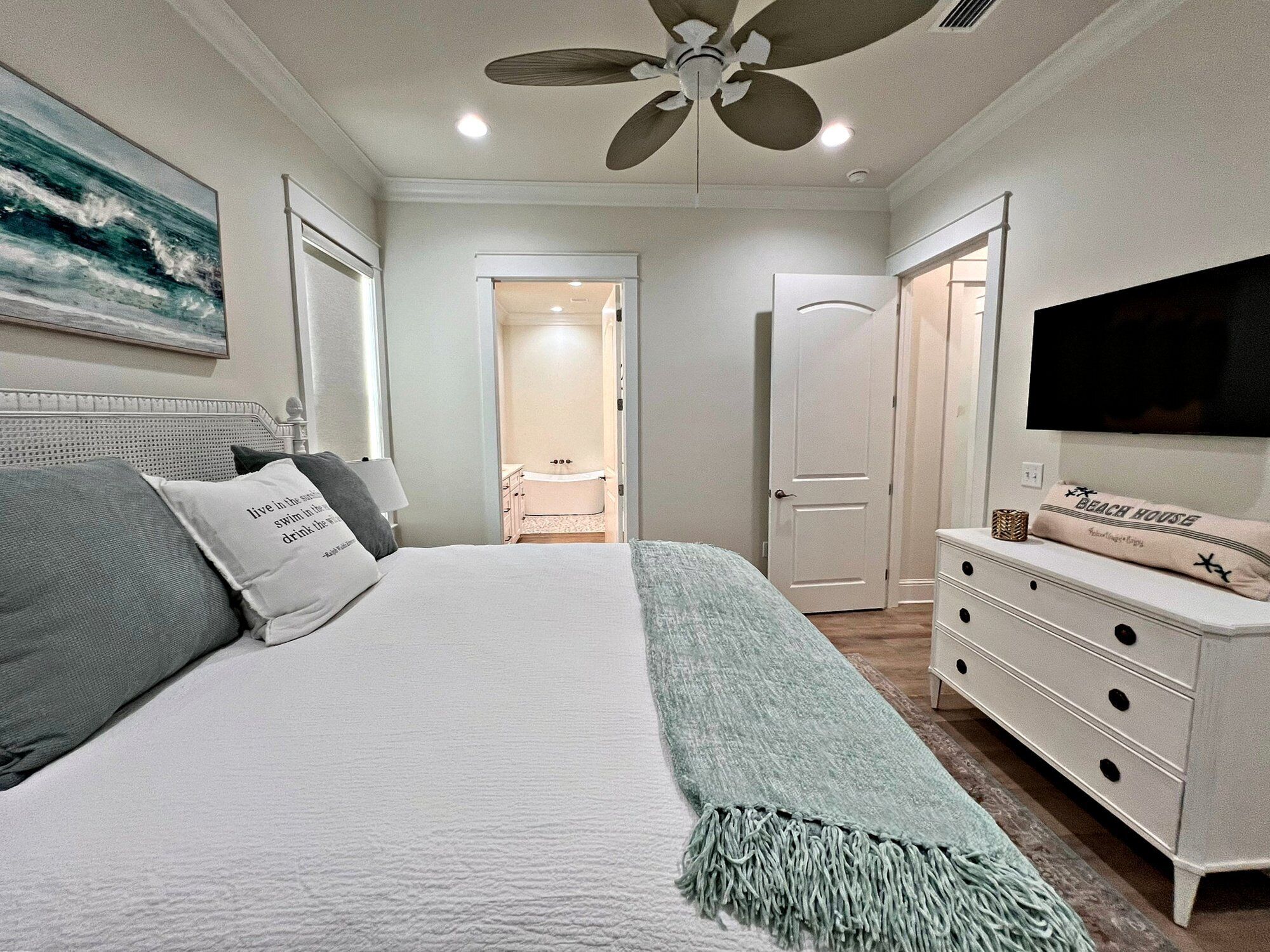 Une chambre à coucher comprenant un lit, une télévision, une commode et une porte donnant sur une salle de bain.