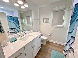 A bathroom with a white sink, mirror, and toilet. There is a blue towel on the floor and a framed picture on the wall. - Southern Coastal (Orange Beach)