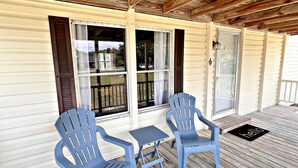 A covered porch with two blue chairs and a small table, wooden deck flooring, and a 'hello' mat. - Oakridge Cottage (Orange Beach)