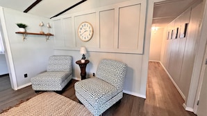 A room with two patterned armchairs, a round wall clock, and a wooden floor. - Oakridge Cottage (Orange Beach)