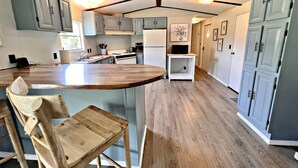 A kitchen with a central island, wooden chairs, and light blue cabinets. - Oakridge Cottage (Orange Beach)