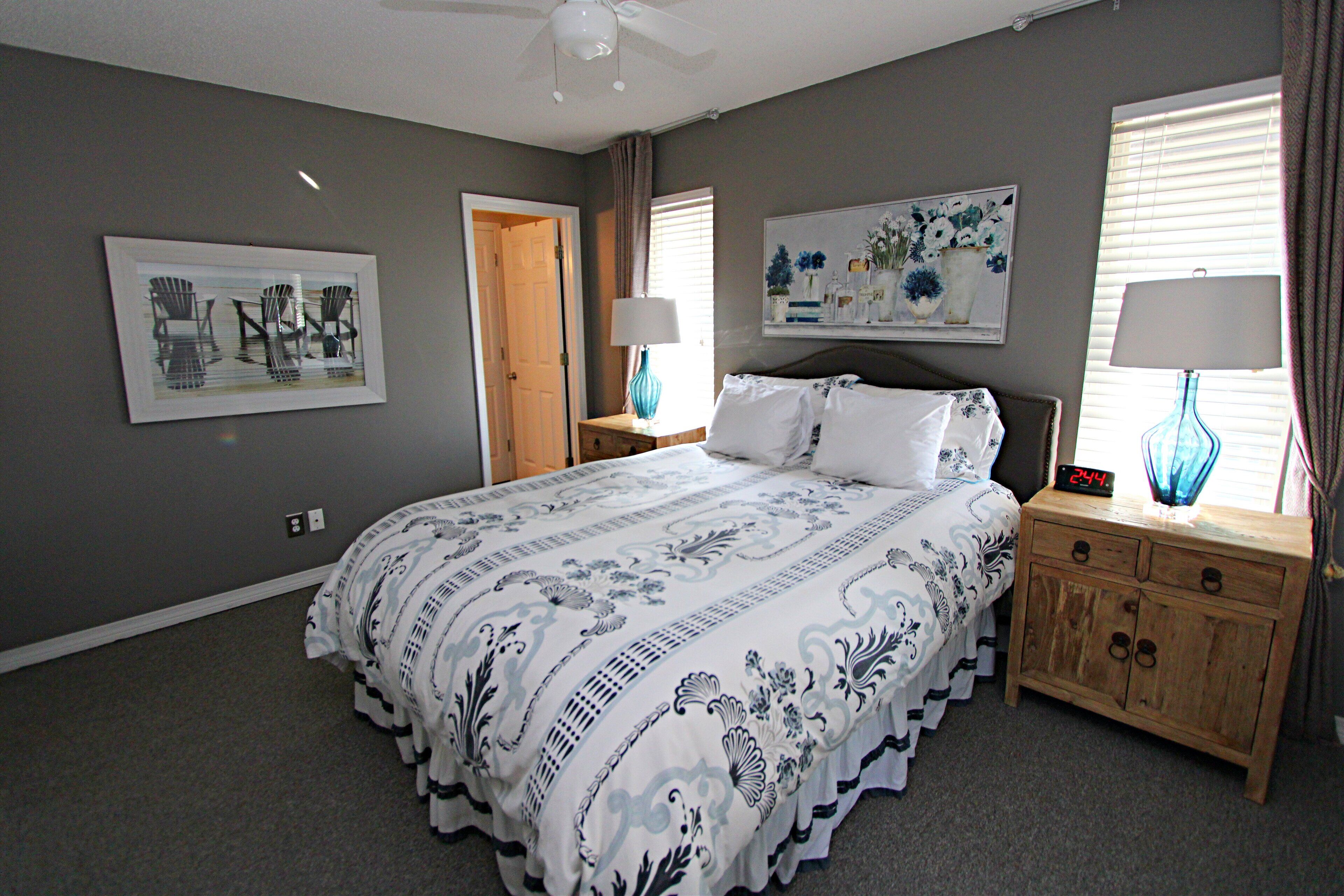 A bedroom with a bed, two nightstands, a ceiling fan, a door, and a wall with a framed picture.