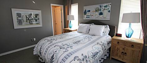 A bedroom with a bed, two nightstands, a ceiling fan, a door, and a wall with a framed picture.