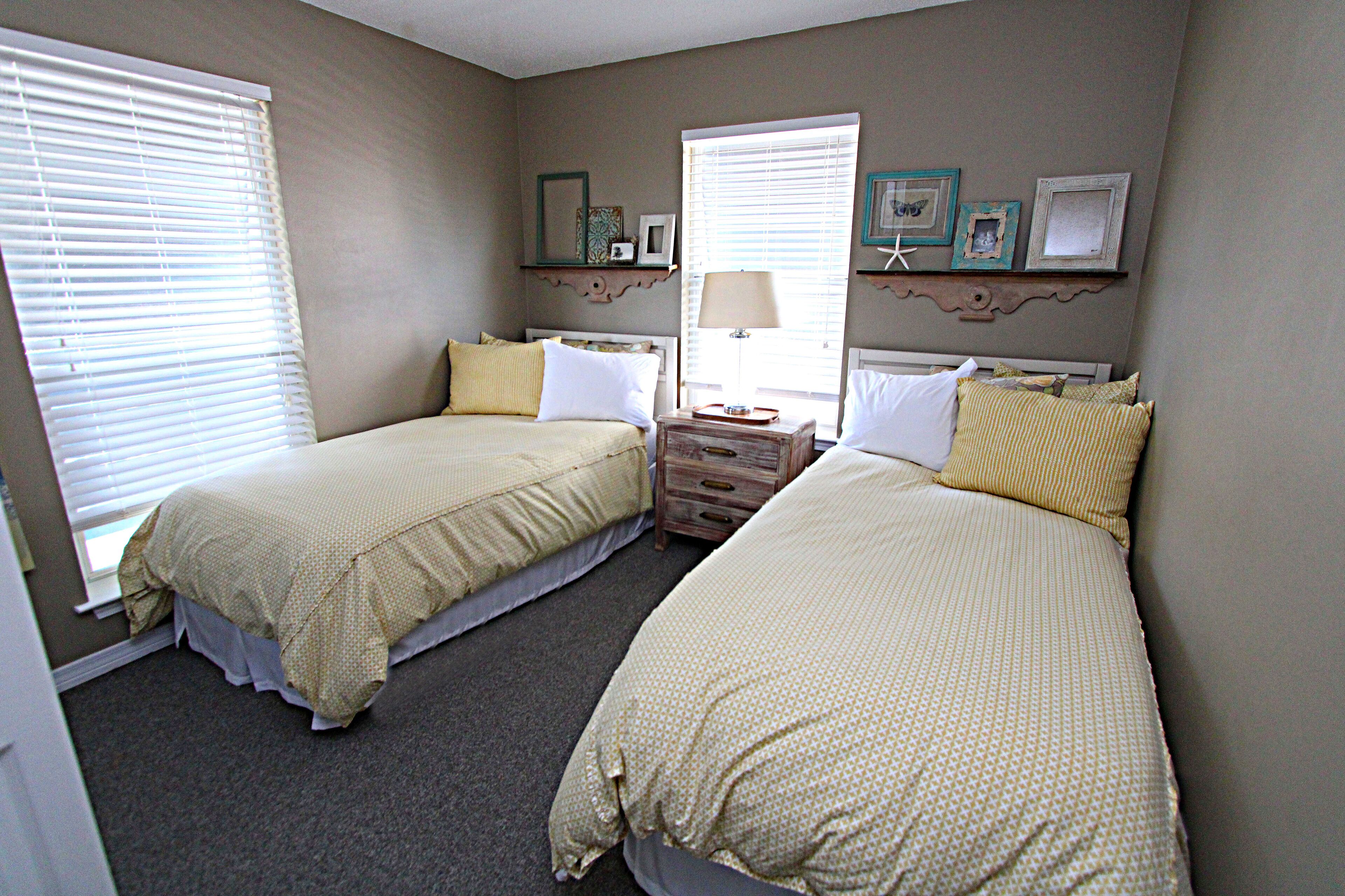 A bedroom with two beds, a dresser, and a window with blinds.
