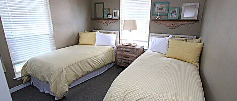 A bedroom with two beds, a dresser, and a window with blinds.