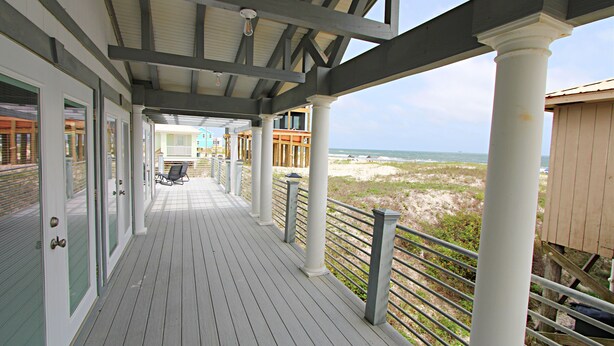 Une terrasse en bois couverte, dotée de rampes blanches, qui offre un accès à une vue sur la plage.