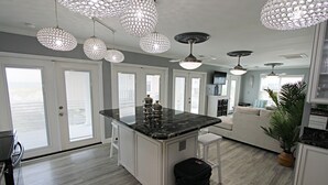 Une cuisine spacieuse dotée d’un îlot central, de luminaires suspendus et donnant sur l’espace de vie.