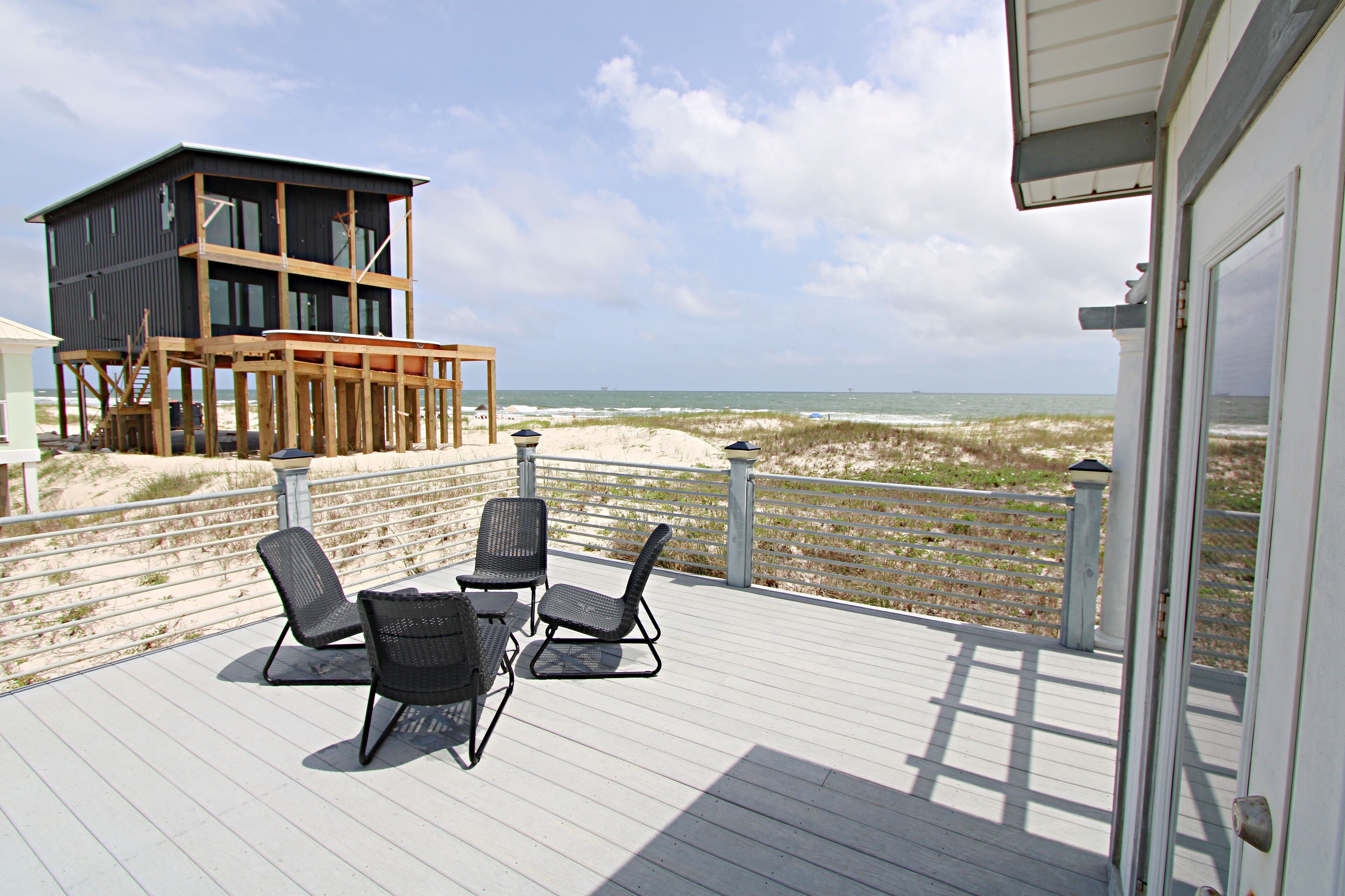 A deck with three chairs and a table, overlooking a beach with a lifeguard tower.