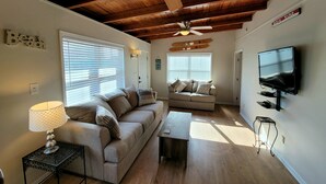 Un salon chaleureux avec un plafond en bois, un ventilateur de plafond, un canapé, une table basse, un téléviseur et une lampe.