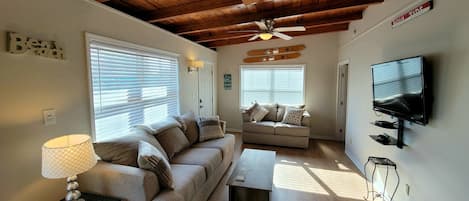 A cozy living room with a wooden ceiling, a ceiling fan, a sofa, a coffee table, a TV, and a lamp.