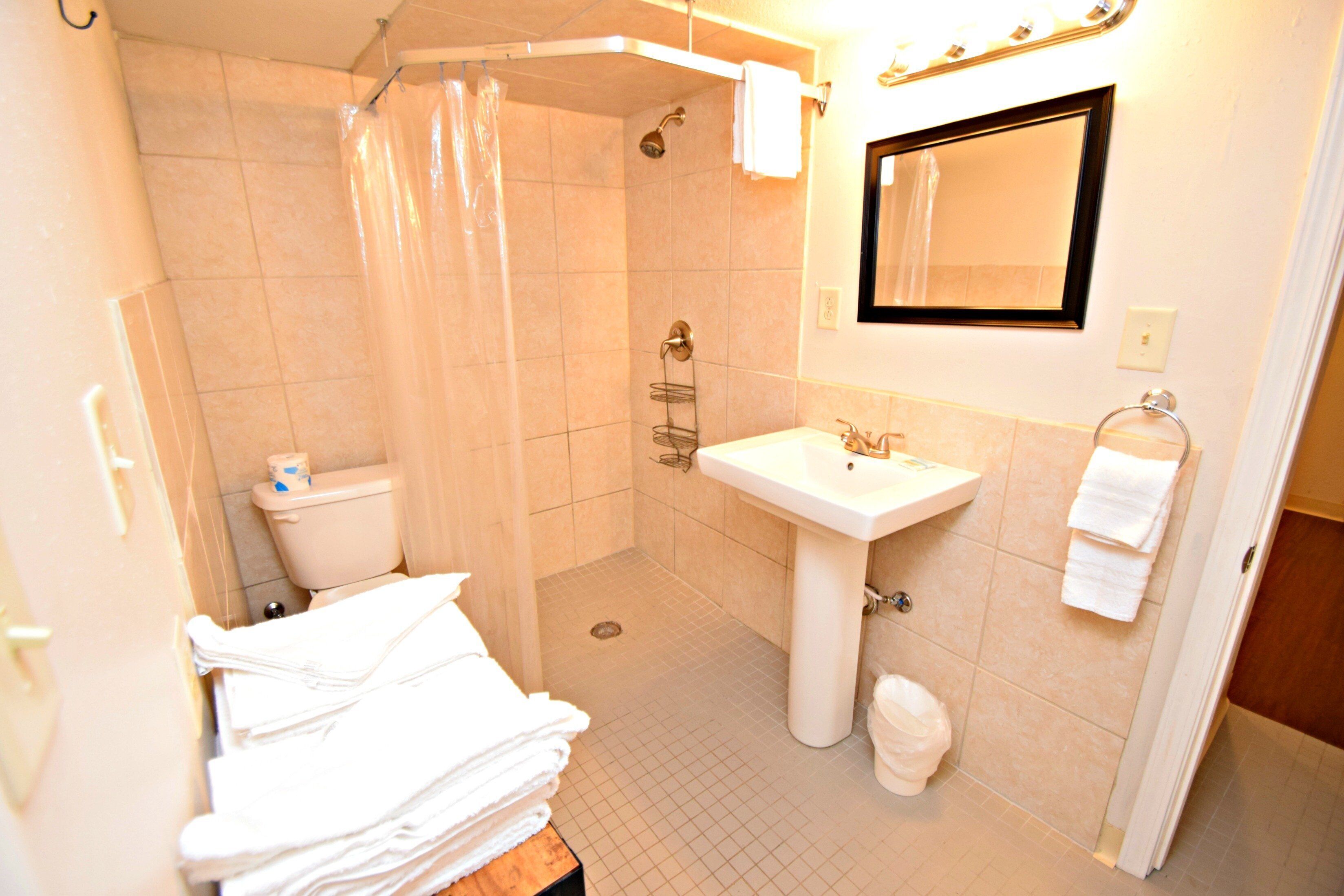 Une salle de bain équipée d’une douche, de toilettes, d’un lavabo et d’une pile de serviettes blanches.