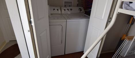 A laundry room with a washing machine and dryer, a bunk bed, and a door leading to another room.