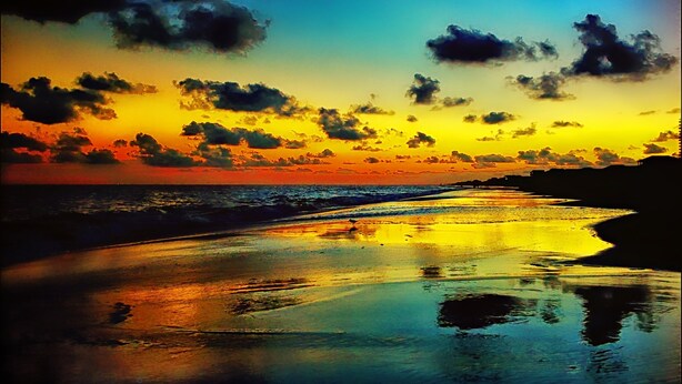 Une plage au coucher du soleil, avec une mer calme et un ciel dégagé.