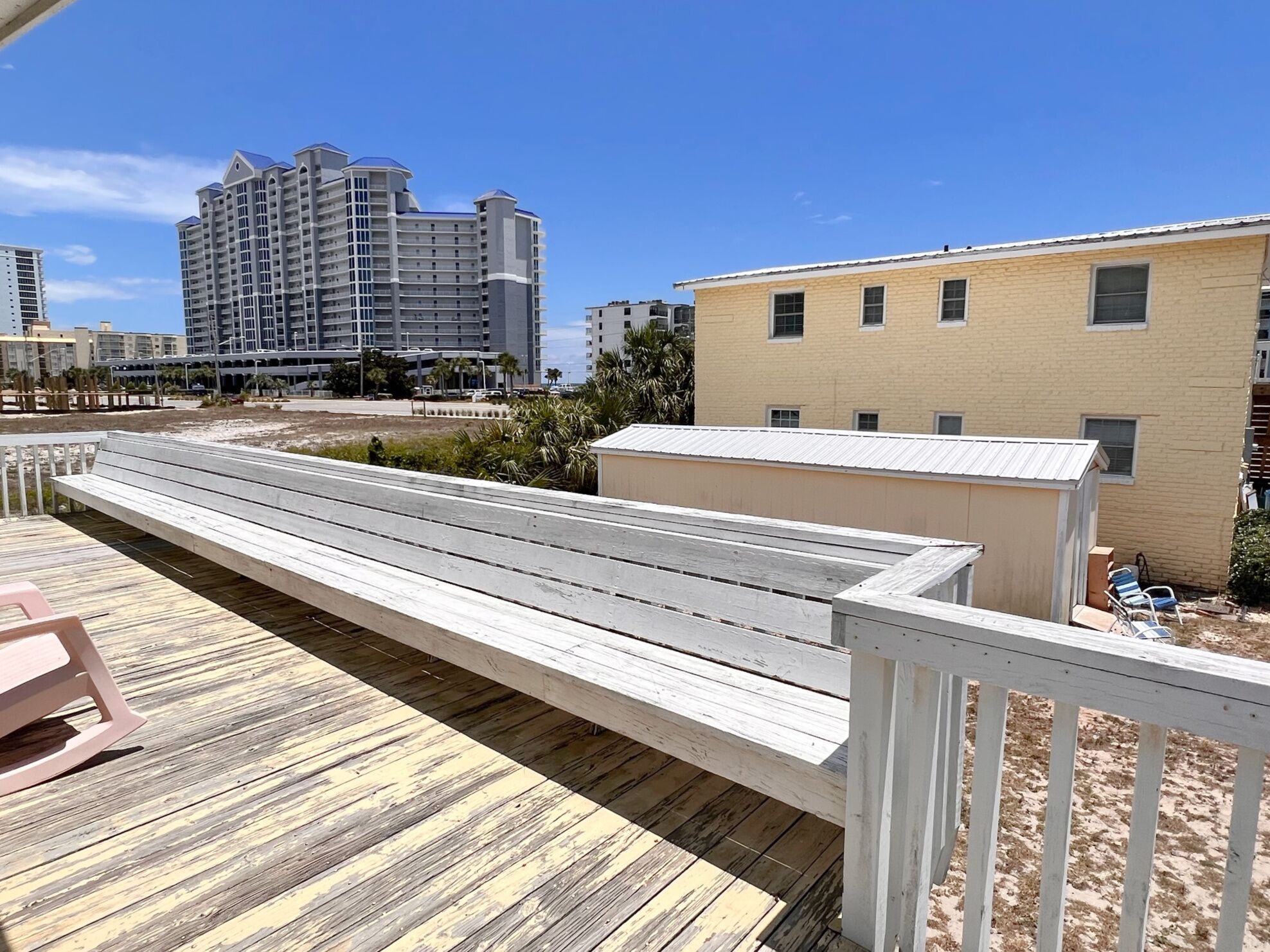 Una terraza de madera con un banco, un cobertizo pequeño y un edificio de techo plano.