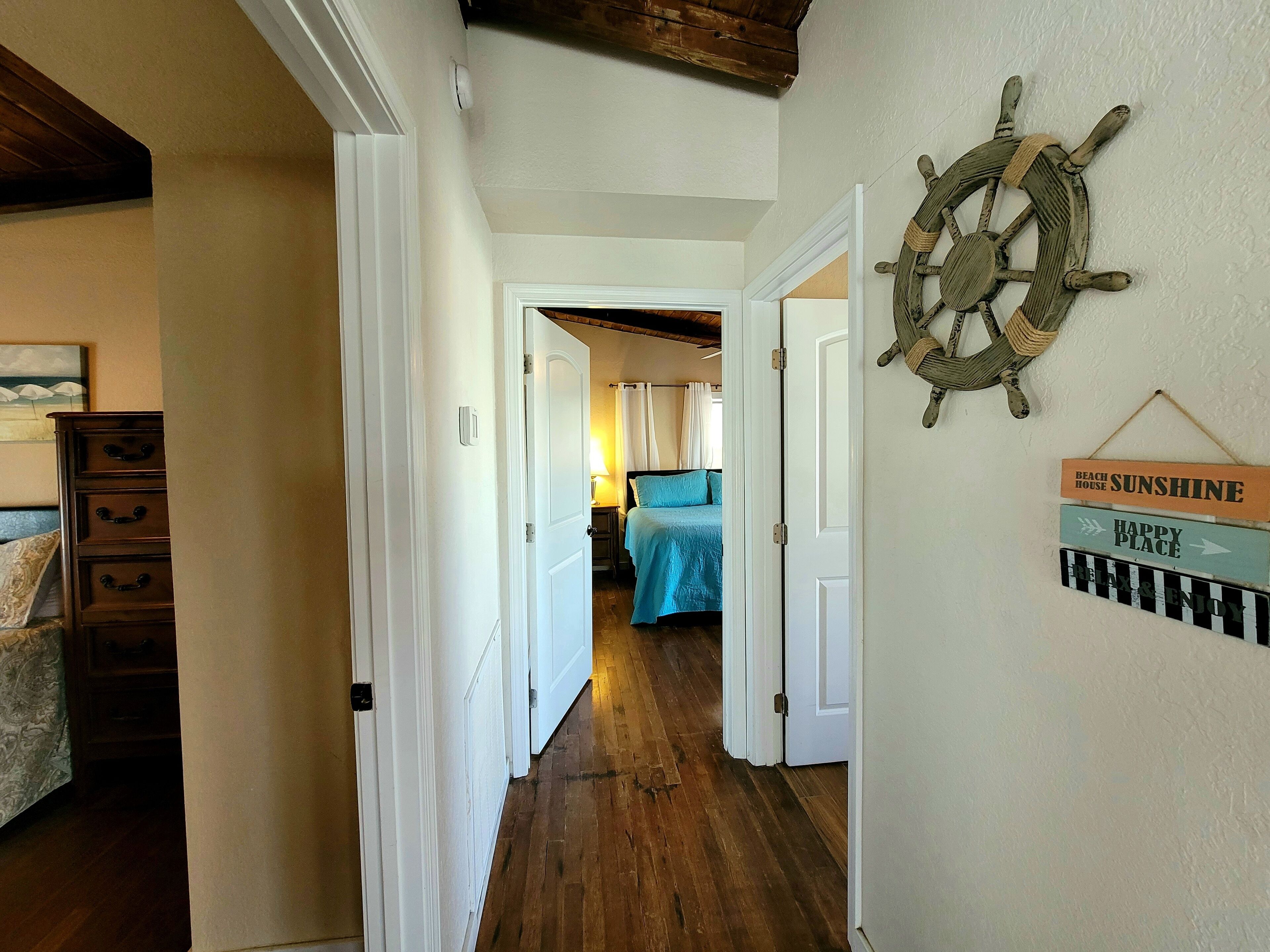 Un corridoio con pavimento in legno, porte bianche e un letto con copripiumino blu.