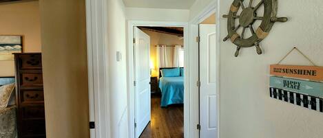 A hallway with wooden flooring, white doors, and a bed with a blue bedspread.