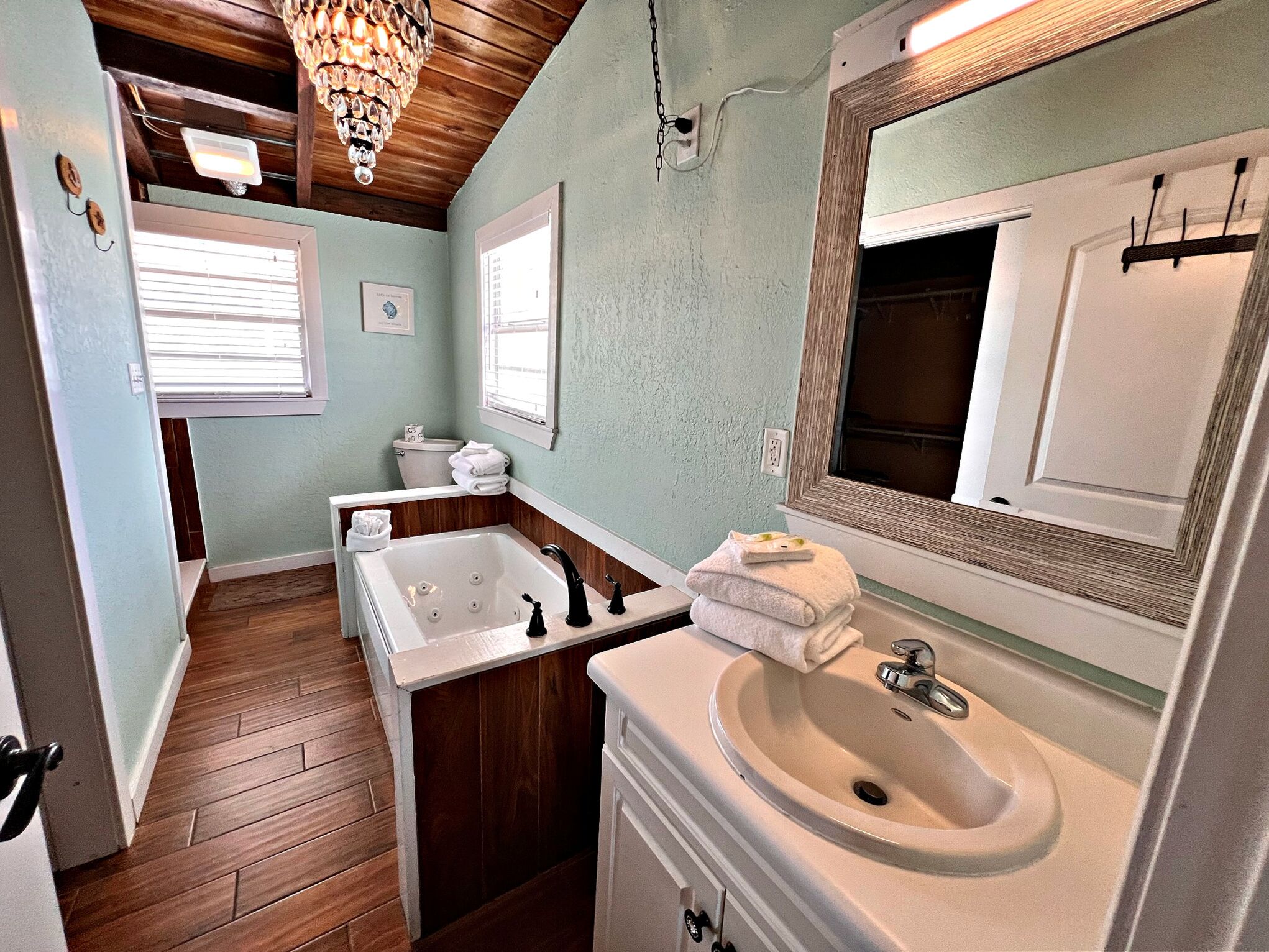 A bathroom with a wooden floor, a white bathtub, a sink, and a mirror.