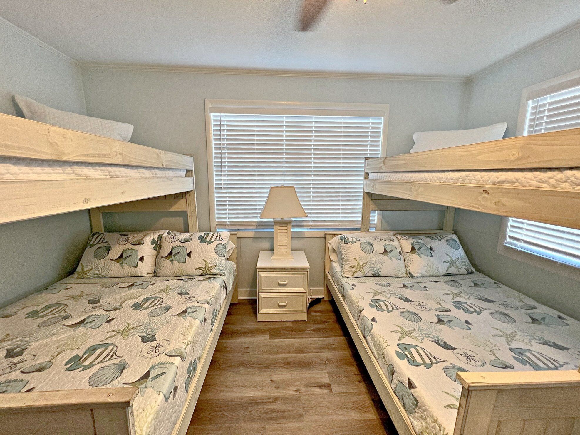 A room with two bunk beds, a bedside table with a lamp, and a window with blinds.