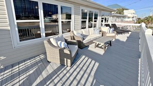 A covered outdoor deck with wicker furniture and a table, overlooking a beach area. - Stay Salty (Gulf Shores)
