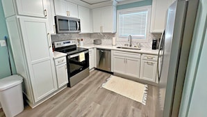 A modern kitchen with white cabinetry, a stainless steel refrigerator, a microwave, a toaster, and a dishwasher. - Stay Salty (Gulf Shores)