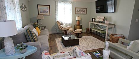 A living room with a sofa, armchair, coffee table, and a television mounted on the wall.