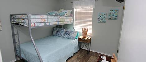 A bunk bed room with a ceiling fan, a small table with a lamp, and artwork on the wall.