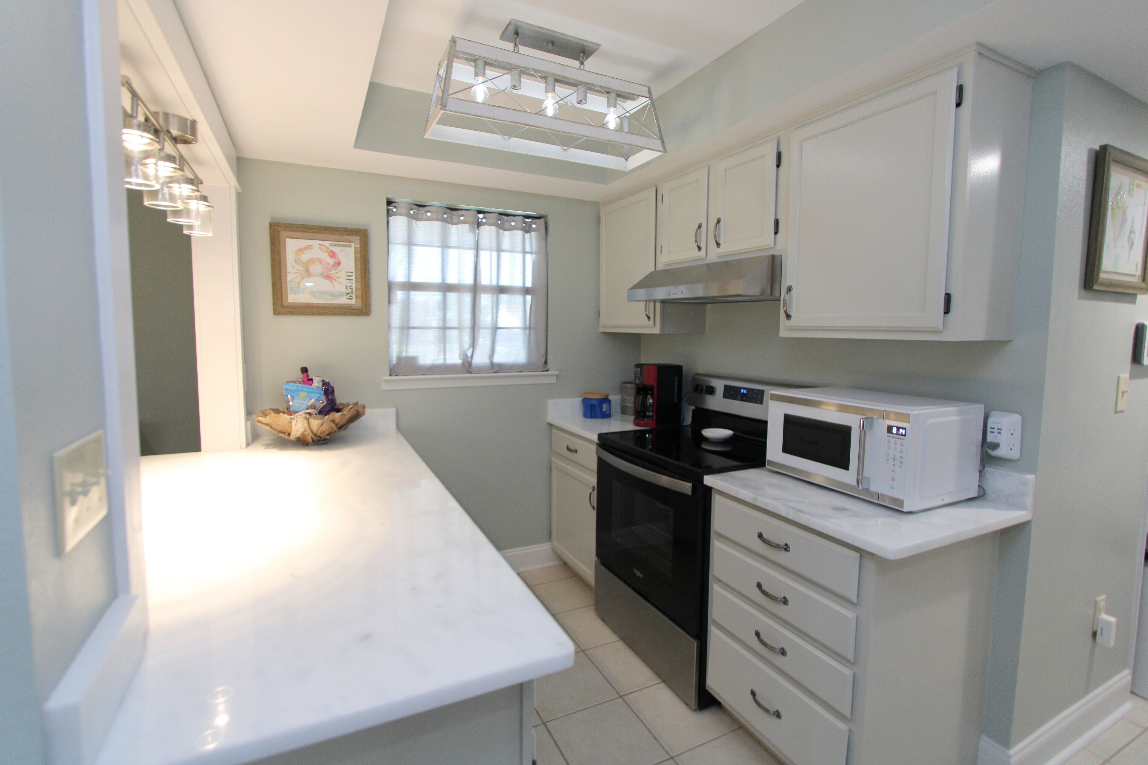 A compact kitchen with white cabinets, a black stove, a microwave, and a window with curtains.