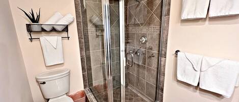 A bathroom with a glass-enclosed shower, a toilet, and a towel rack with multiple towels.