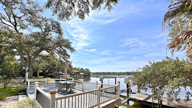 A wooden deck with a railing overlooking a calm lake, surrounded by trees and a gazebo. - Porpoise Pass - Ground Floor Guest Suite (Foley)