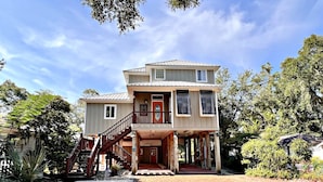 A two-story building with a wooden staircase leading to the entrance, surrounded by trees and a gravel driveway. - Porpoise Pass - Ground Floor Guest Suite (Foley)