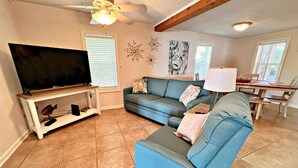 A living room with a television, a blue sofa, a dining table, and a ceiling fan. - Porpoise Pass - Ground Floor Guest Suite (Foley)