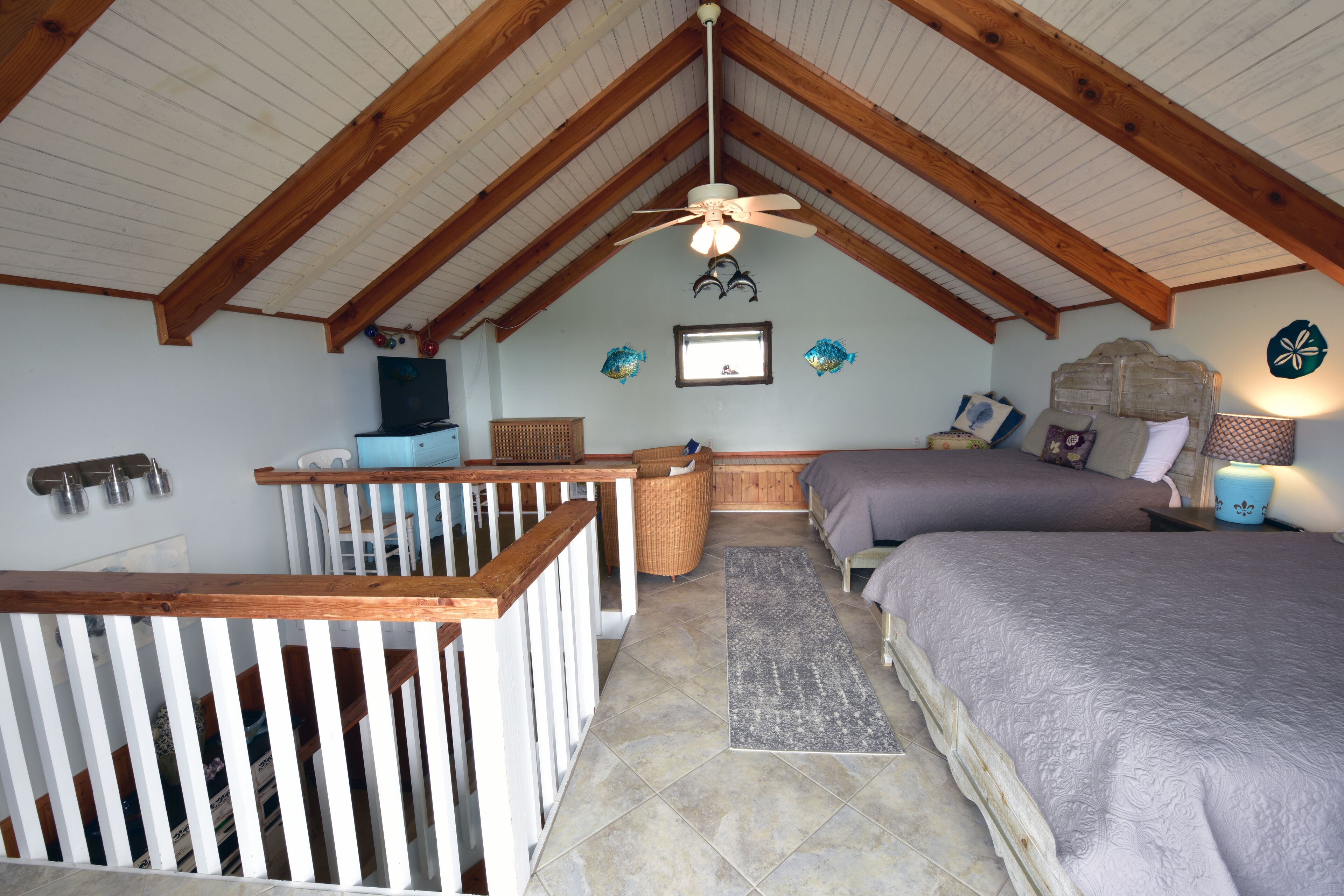 Um quarto com teto inclinado, vigas de madeira, uma cama, uma escrivaninha e uma cadeira.