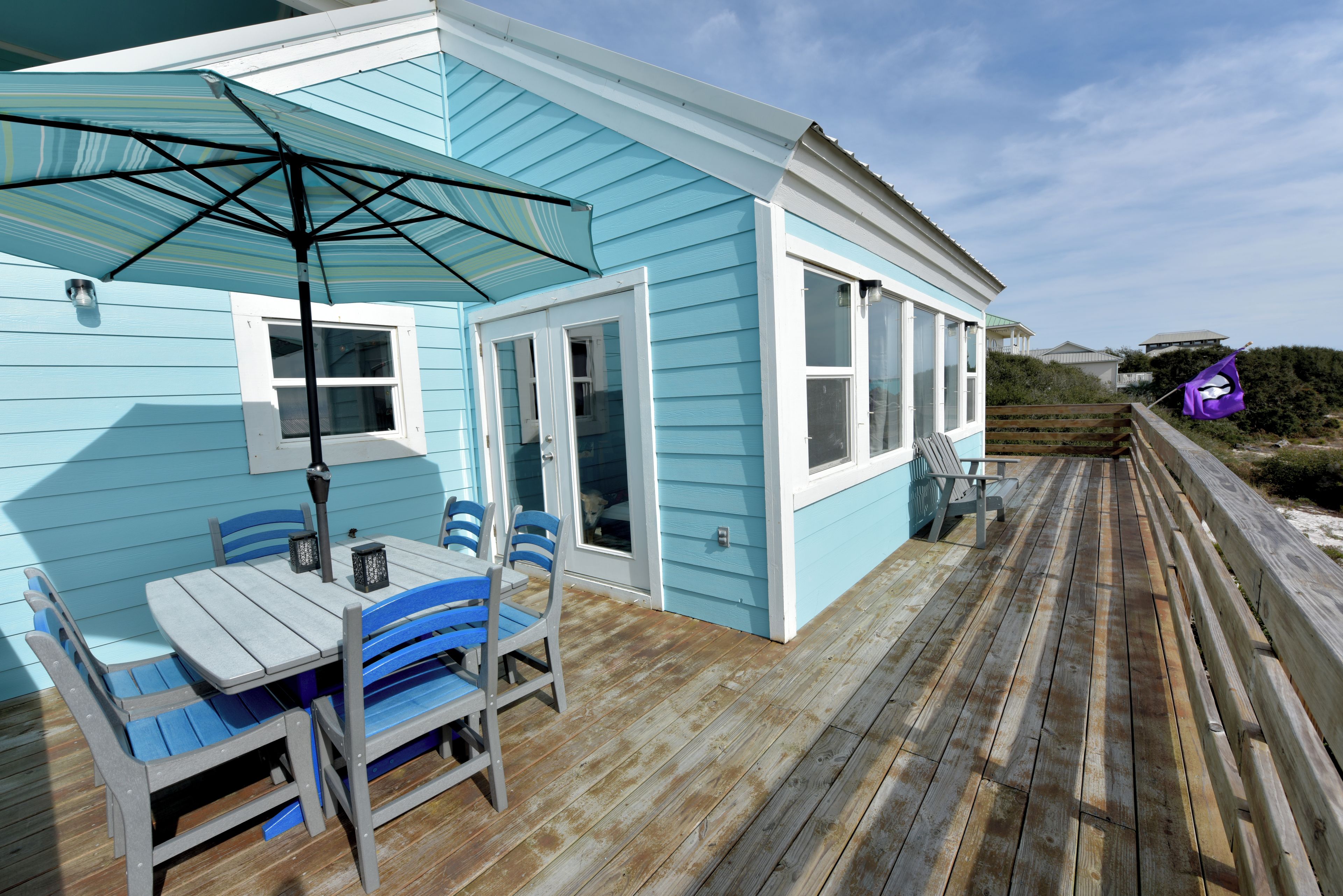 Une terrasse en bois avec une table et des chaises, un parasol et une vue sur l’océan.