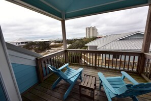 A covered balcony with two blue Adirondack chairs and a small table.