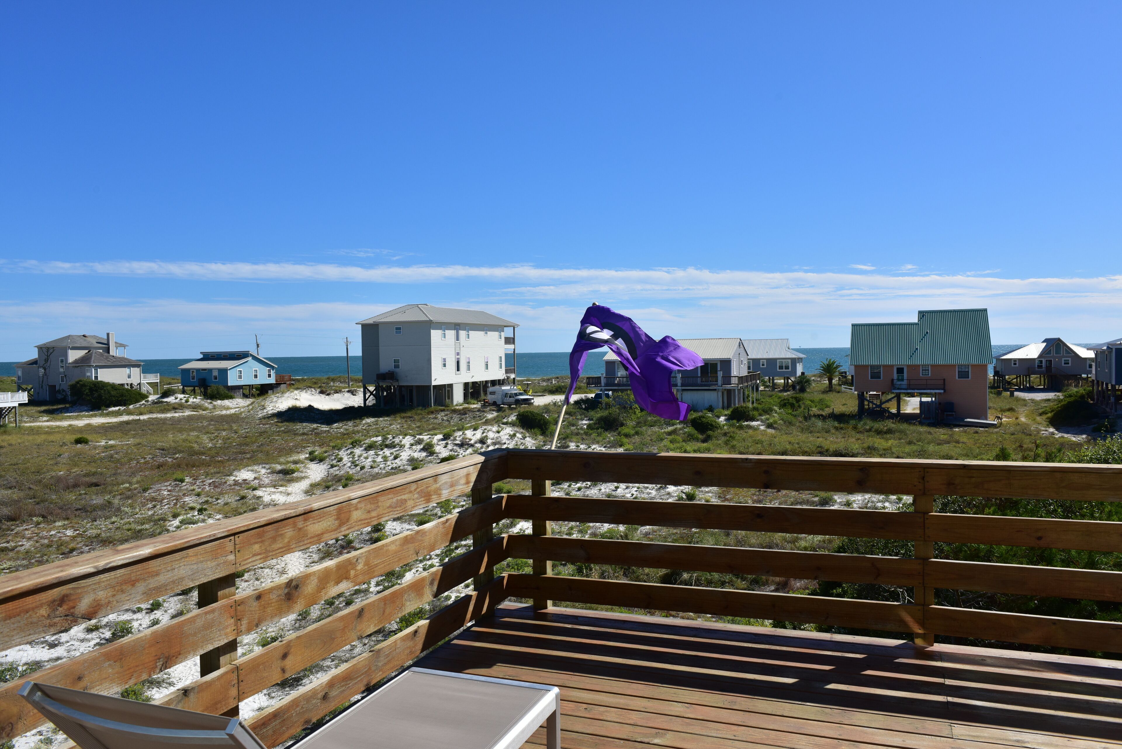 A wooden deck with a bench overlooking a beach with houses and the ocean.