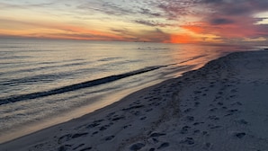 Ranta, jossa näkyy jalanjälkiä, jotka johtavat veteen, tyyni meri ja auringonlaskun värittämä taivas.