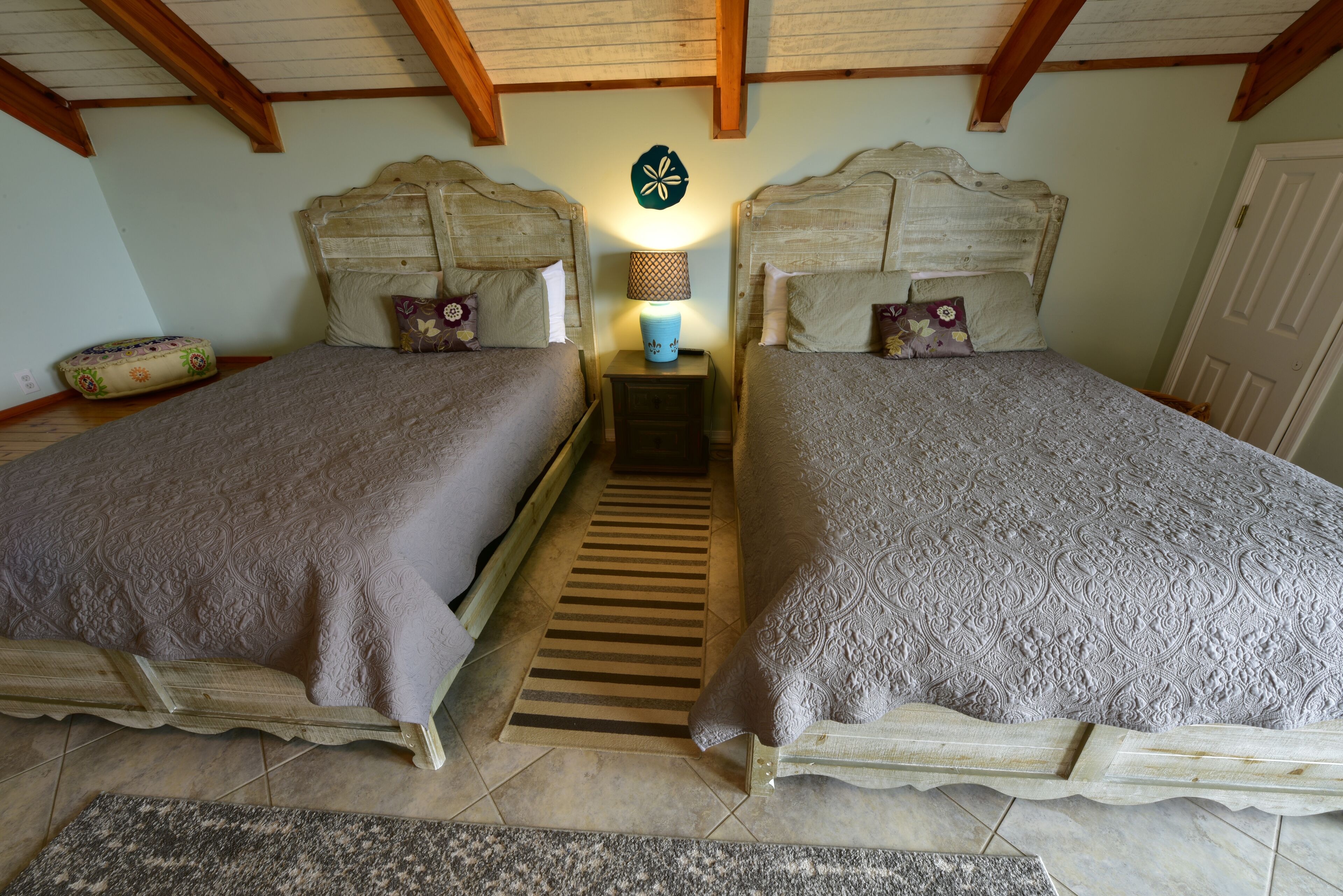 A bedroom with two beds, wooden headboards, a nightstand with a lamp, and a decorative wall piece.