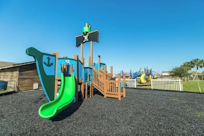 Un parque infantil con un tobogán verde, una estructura de juego temática de piratas y un tobogán amarillo.