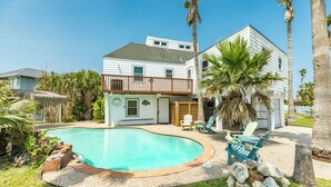 Ein zweistöckiges Haus mit Swimmingpool, Balkon und einer Terrasse mit Sitzgelegenheiten.