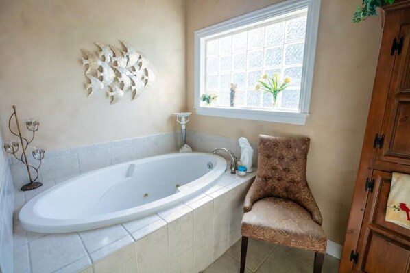 A bathroom with a large bathtub, a window with flowers, and a decorative wall piece.