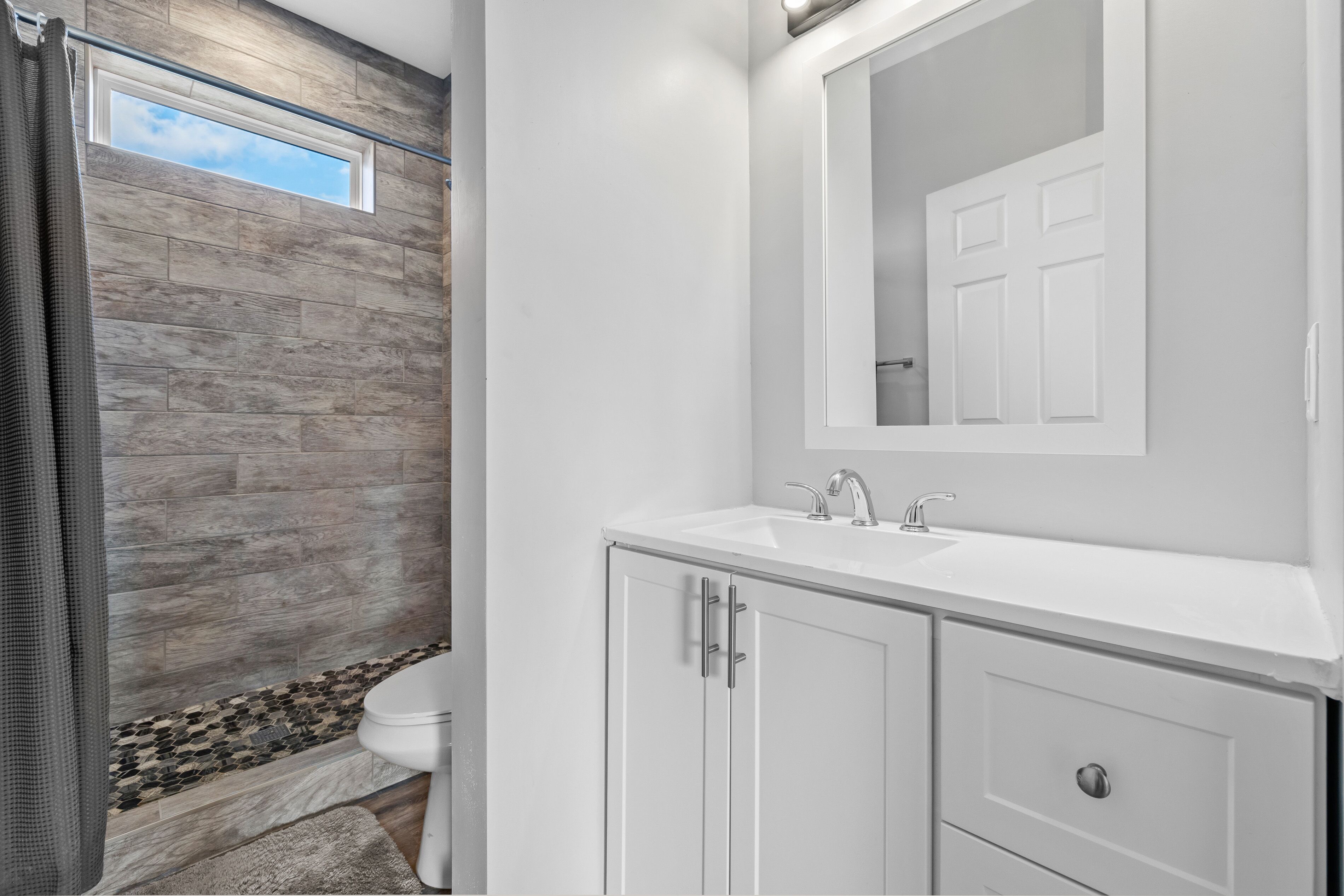 A bathroom with a stone wall, a white sink, and a mirror above it.
