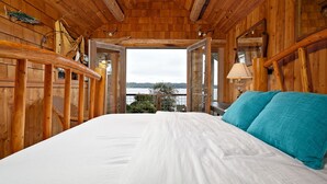 Une chambre dans une cabane en bois, avec un lit, une vue sur un lac et un plafond en bois.